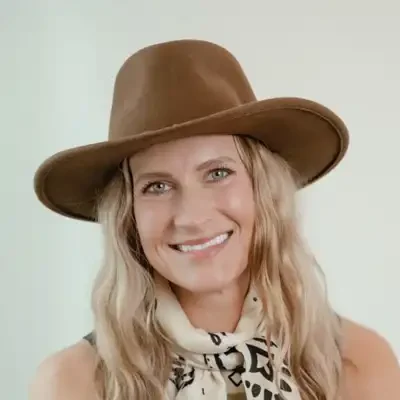 Chiropractor Holmen WI Portrait of Amanda with long wavy hair wearing a wide-brim brown hat and a patterned light-colored scarf Meet The Team